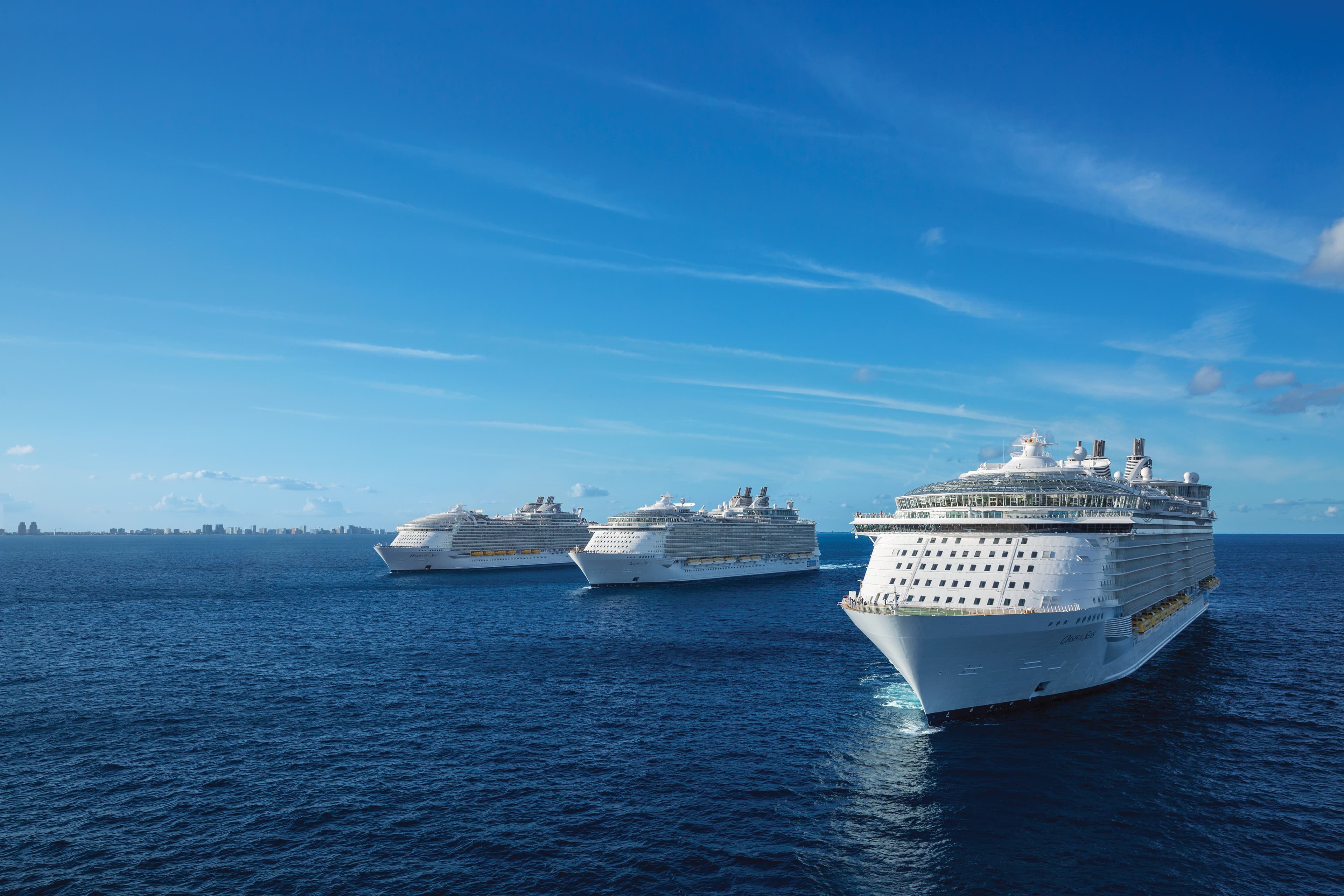 Три круизных лайнера Royal Caribbean плывут строем по открытому океану под ясным синим небом.